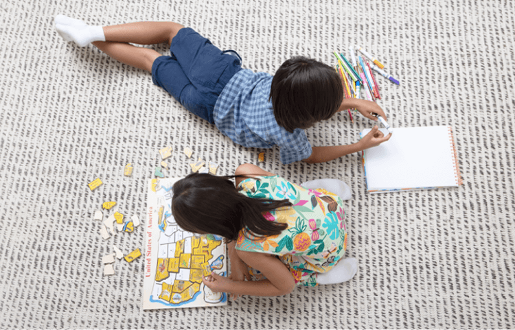 Overhead view of two young children playing with a puzzle, and drawing on a rug.